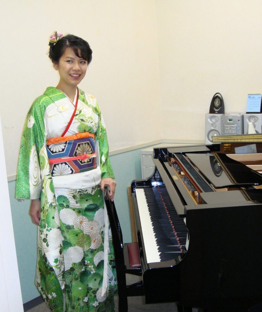 West Vancouver's piano teacher Yuki  is wearing her kimono and standing in front of a grand piano at a piano studio in Japan.